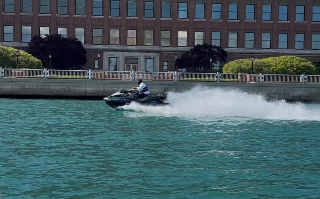 Jet ski carving past the Detroit riverfront with a wake spray