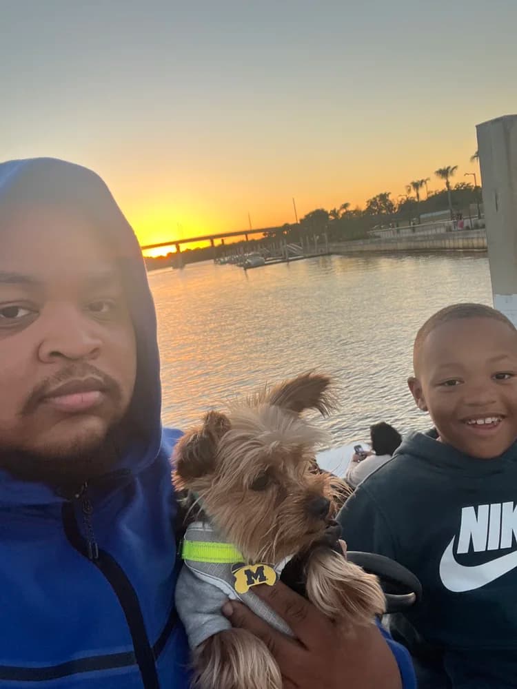 Josh, his son Junior, and their dog at the waterfront at sunset