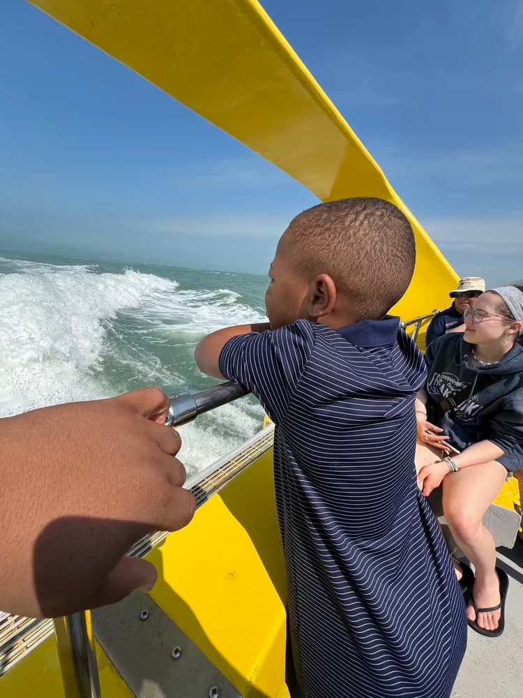 Junior leaning on a boat railing watching the wake on open water